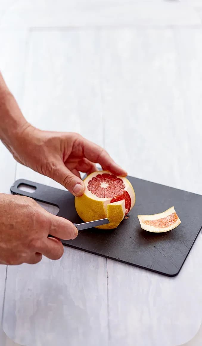 Chef peeling a grapefruit on a black board