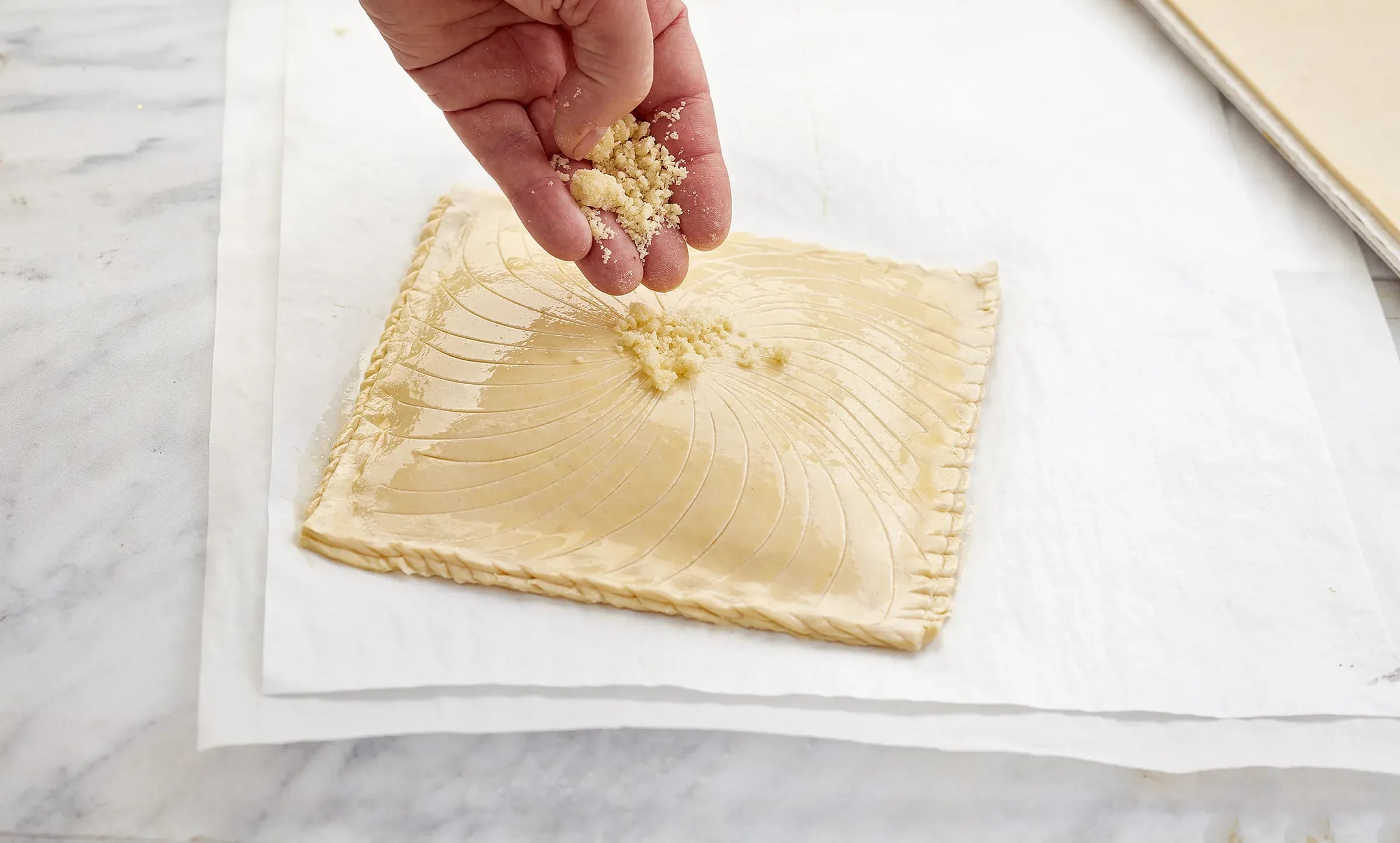 Hand sprinkling almond crumble on a puff pastry square